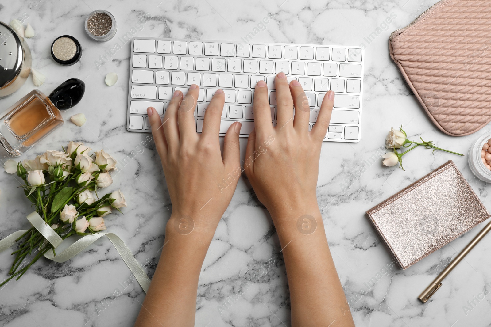 Photo of Woman typing on keyboard at table with beautiful roses, top view