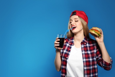 Pretty woman with tasty burger and cola on color background. Space for text