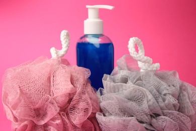 Photo of Colorful shower puffs and bottle of cosmetic product on pink background, closeup