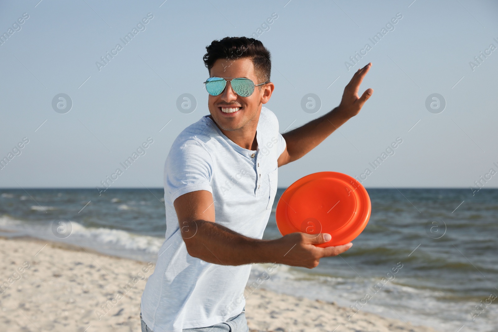 Photo of Happy man throwing flying disk at beach on sunny day