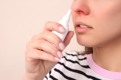 Woman using nasal spray on beige background, closeup. Space for text