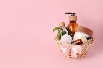 Photo of Spa gift set of different luxury products in wicker basket on pale pink background, space for text