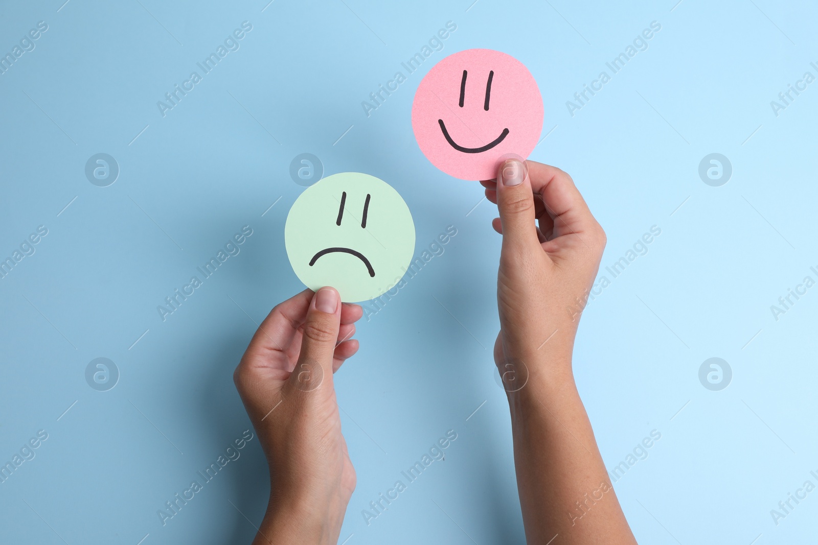 Photo of Choice concept. Woman holding papers with sad and happy emoticons on light blue background, top view