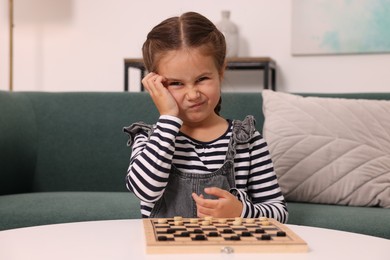 Thoughtful girl playing checkers on sofa at home