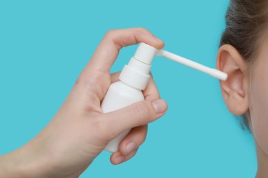 Mother spraying medication into daughter's ear on light blue background, closeup