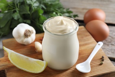 Photo of Fresh mayonnaise sauce in glass jar and ingredients on wooden table, closeup