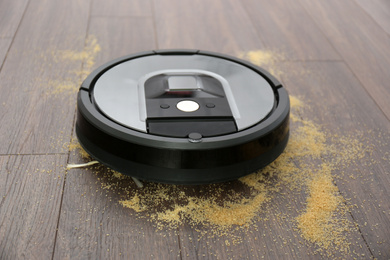 Modern robotic vacuum cleaner removing scattered groats from wooden floor