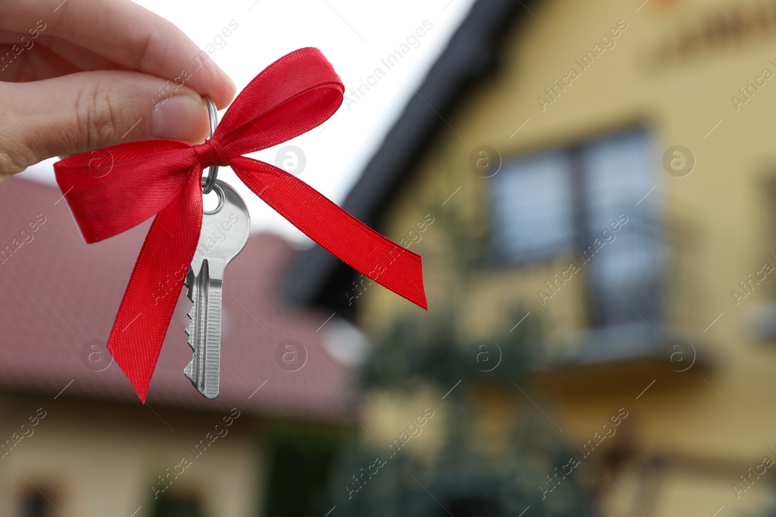 Photo of Woman holding key with bow near house outdoors, closeup. Space for text