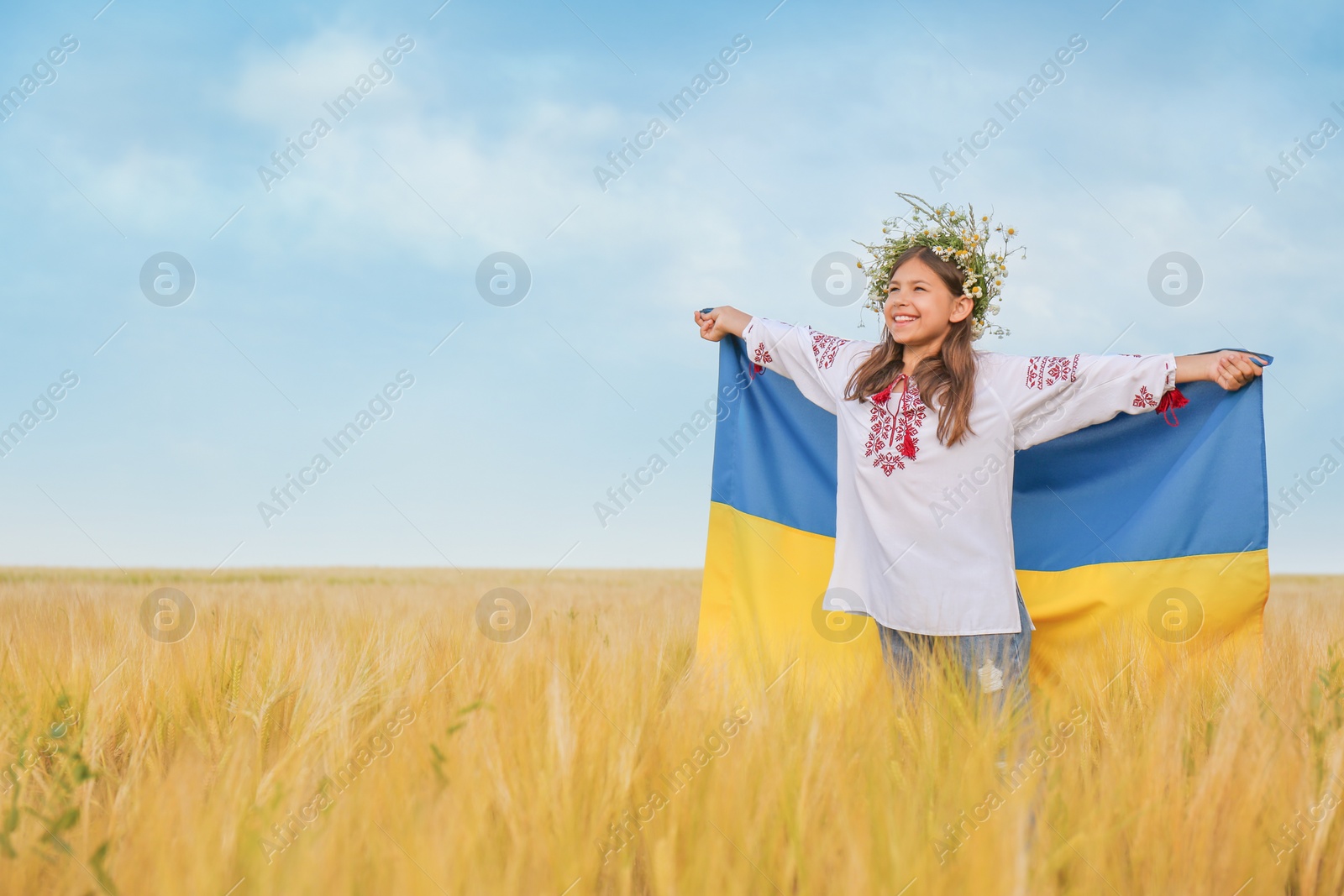 Photo of Happy little girl with national flag of Ukraine in wheat field. Space for text