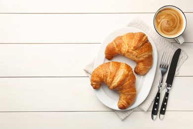 Delicious fresh croissants served with coffee on white wooden table, flat lay. Space for text