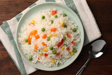 Delicious rice with vegetables and spoon on wooden table, flat lay