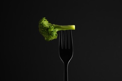 Fork with tasty broccoli on black background