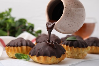 Pouring chocolate cream onto delicious profiterole on white table, closeup