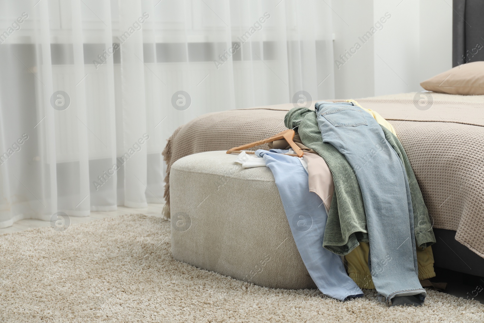 Photo of Many different clothes on ottoman in bedroom, space for text