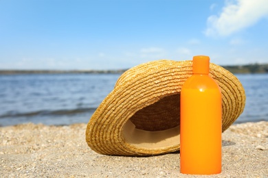 Photo of Bottle of sun protection body cream and hat on beach, space for design