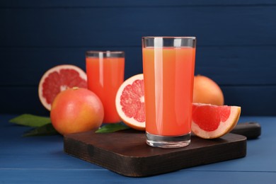 Photo of Tasty grapefruit juice in glass and fresh fruits on blue wooden table