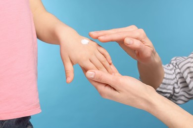 Mother applying ointment onto her daughter's hand on light blue background, closeup