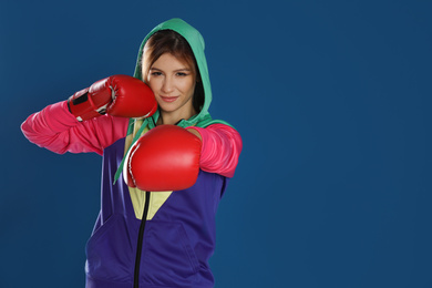 Young woman with boxing gloves on blue background, space for text