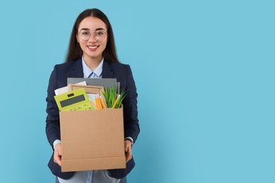 Photo of Happy unemployed woman with box of personal office belongings on light blue background, space for text