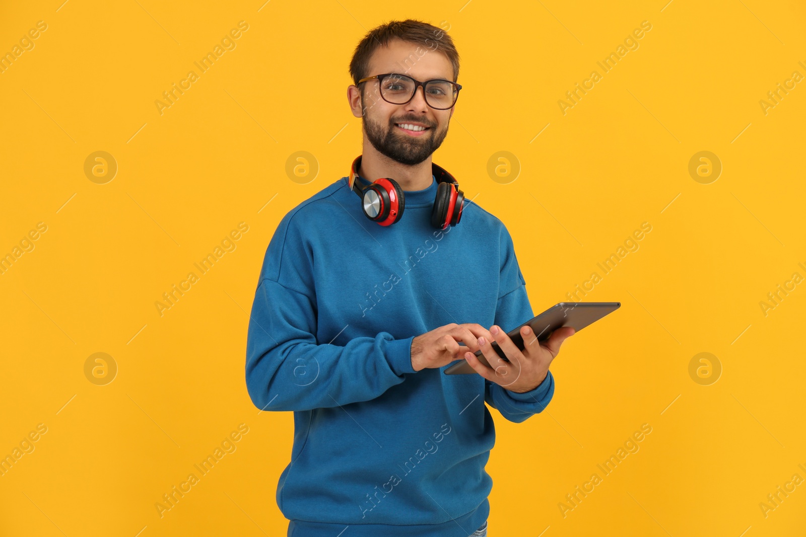 Photo of Student with headphones using tablet on yellow background