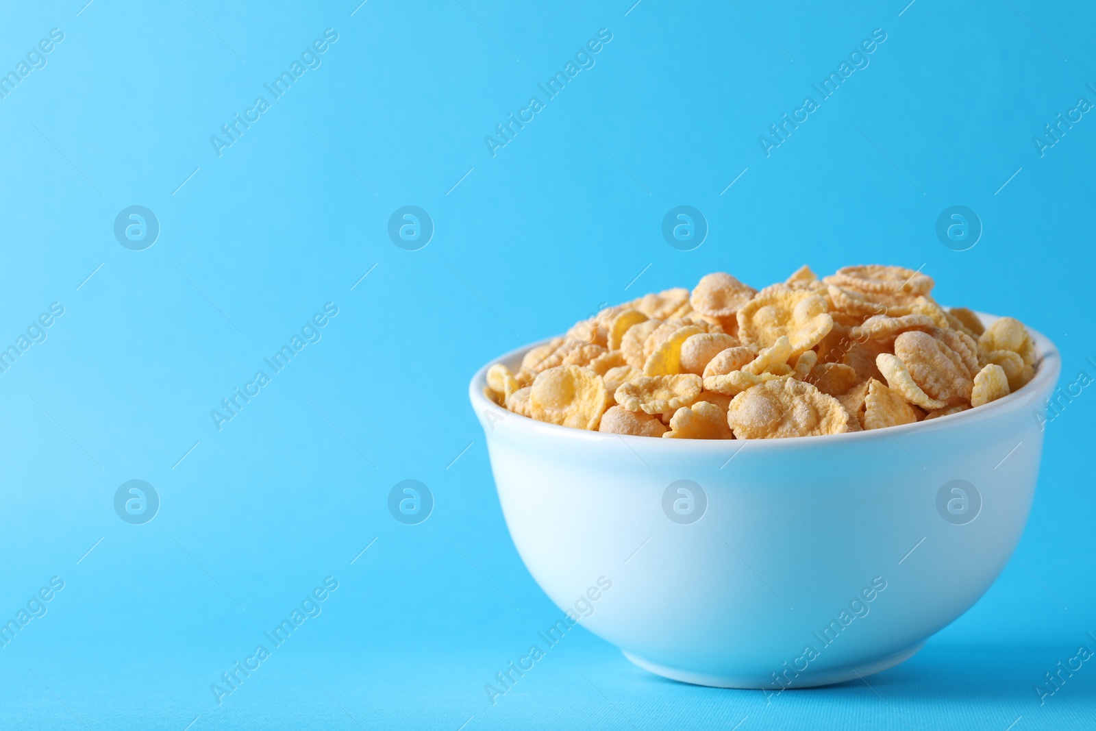 Photo of Bowl of tasty crispy corn flakes on light blue background, space for text