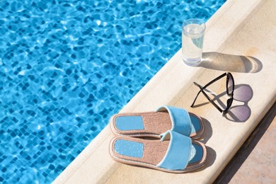 Photo of Stylish sunglasses, slippers and glass of water at poolside on sunny day, space for text. Beach accessories