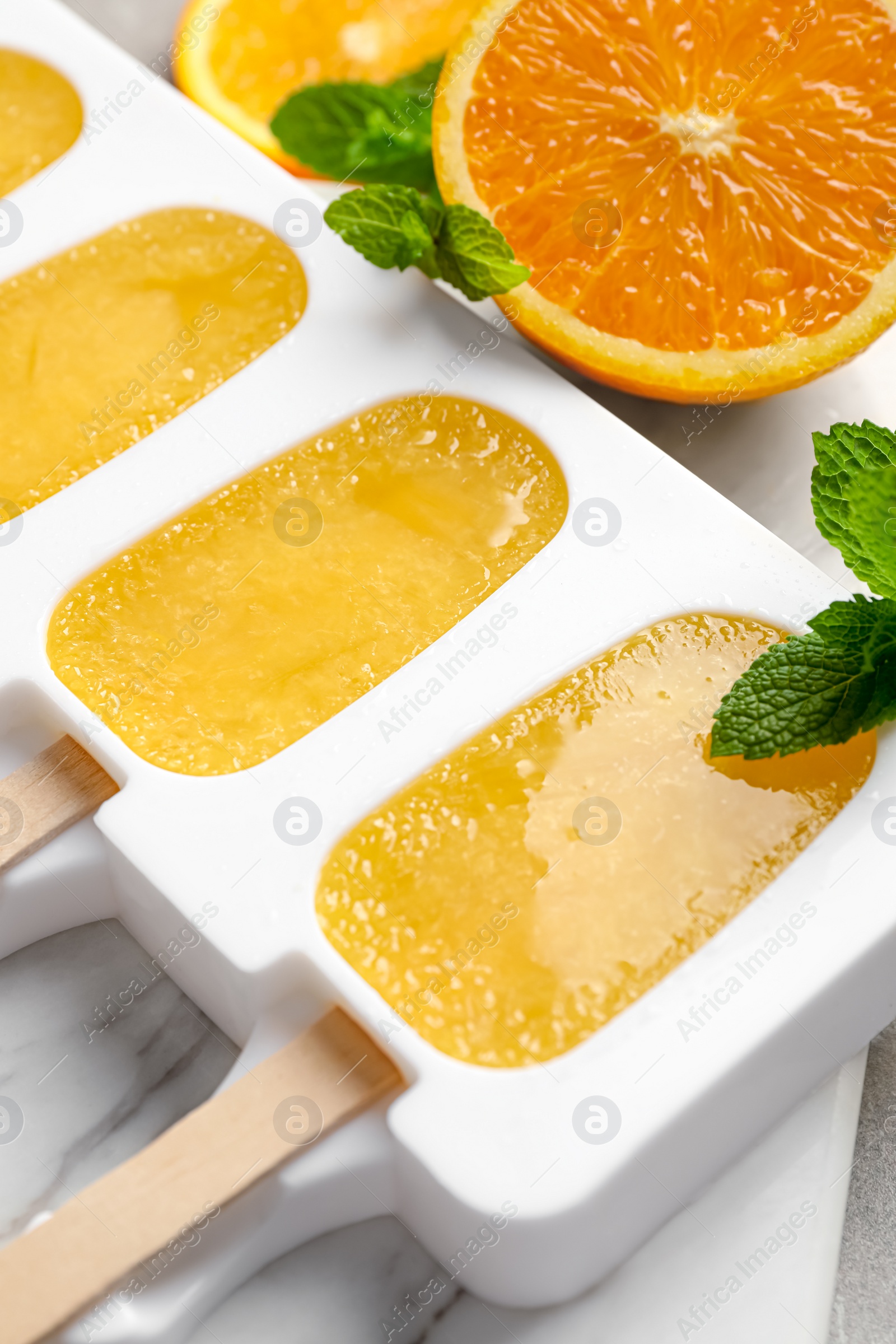Photo of Tasty orange ice pops in mold on table, closeup. Fruit popsicle