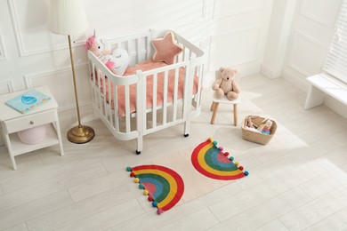 Stylish rug with rainbow on floor in baby room, above view