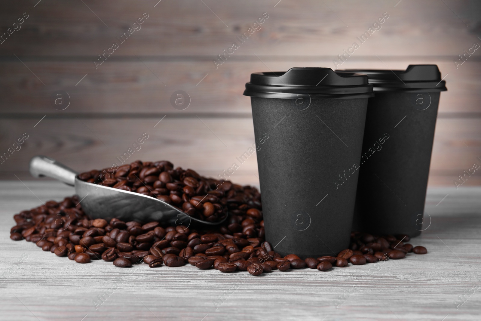 Photo of Coffee to go. Paper cups, roasted beans and scoop on light wooden table