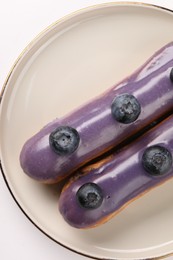 Photo of Delicious eclairs decorated with blueberries on white background, top view