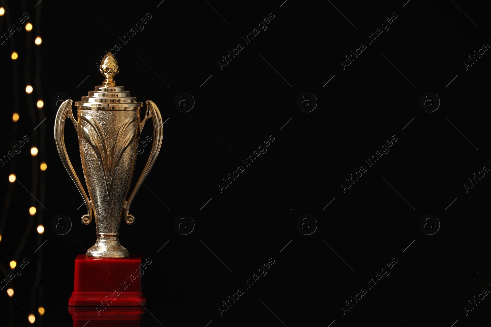 Photo of Golden trophy cup against blurred festive lights, space for text