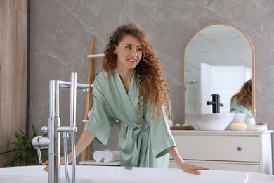 Photo of Beautiful woman in green silk robe near bathtub at home