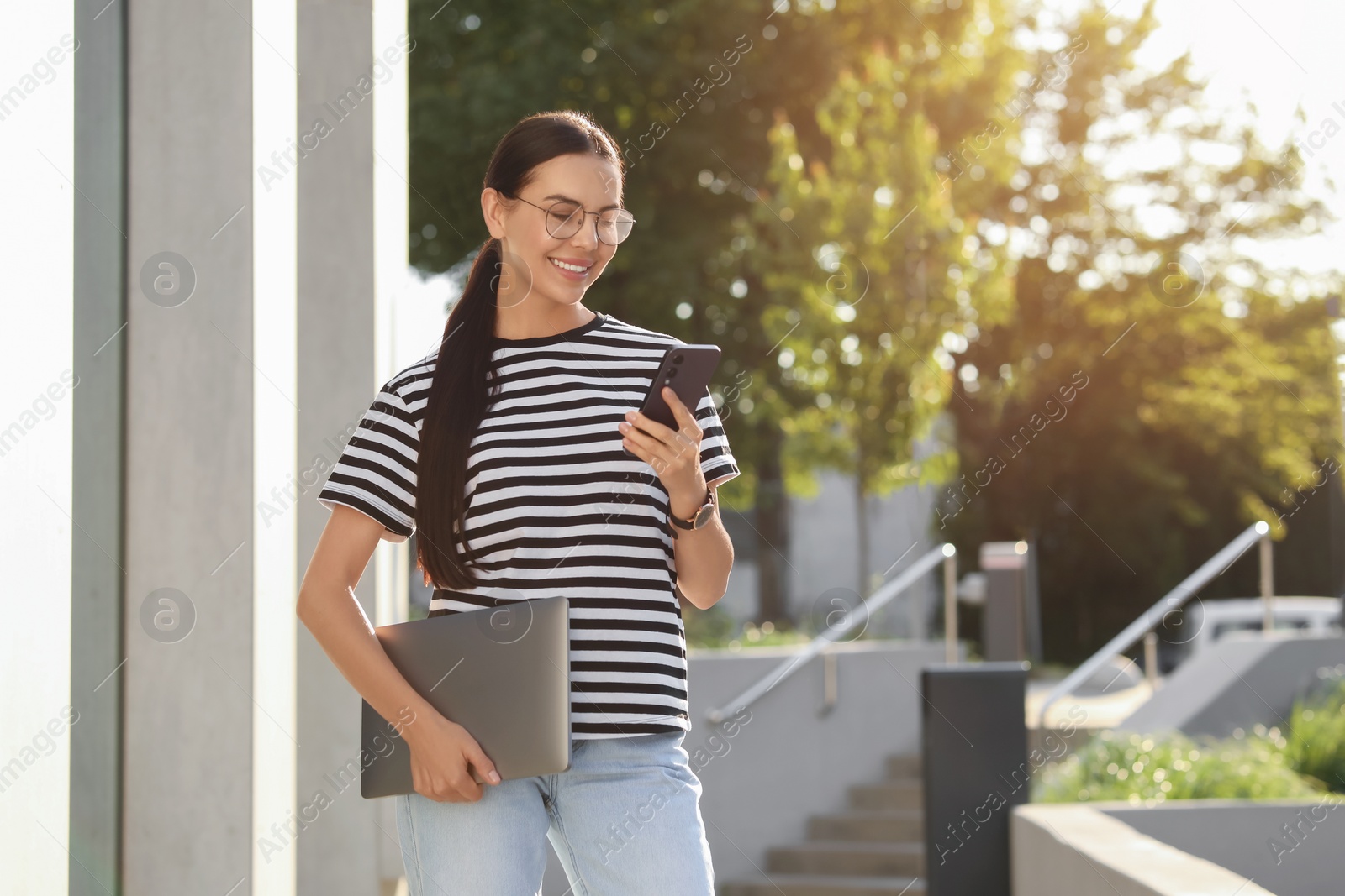 Photo of Happy young woman with modern laptop using smartphone outdoors. Space for text