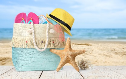 Image of Bag with accessories and starfish on sunny ocean beach, space for text. Summer vacation