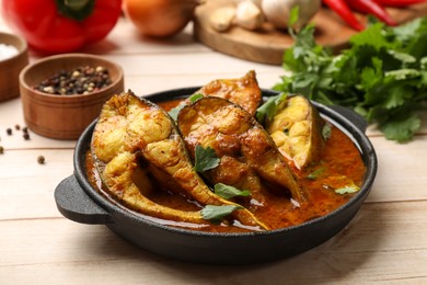 Photo of Tasty fish curry and ingredients on white wooden table, closeup. Indian cuisine