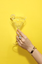 Photo of Woman holding martini glass of refreshing cocktail with lemon slice on yellow background, closeup