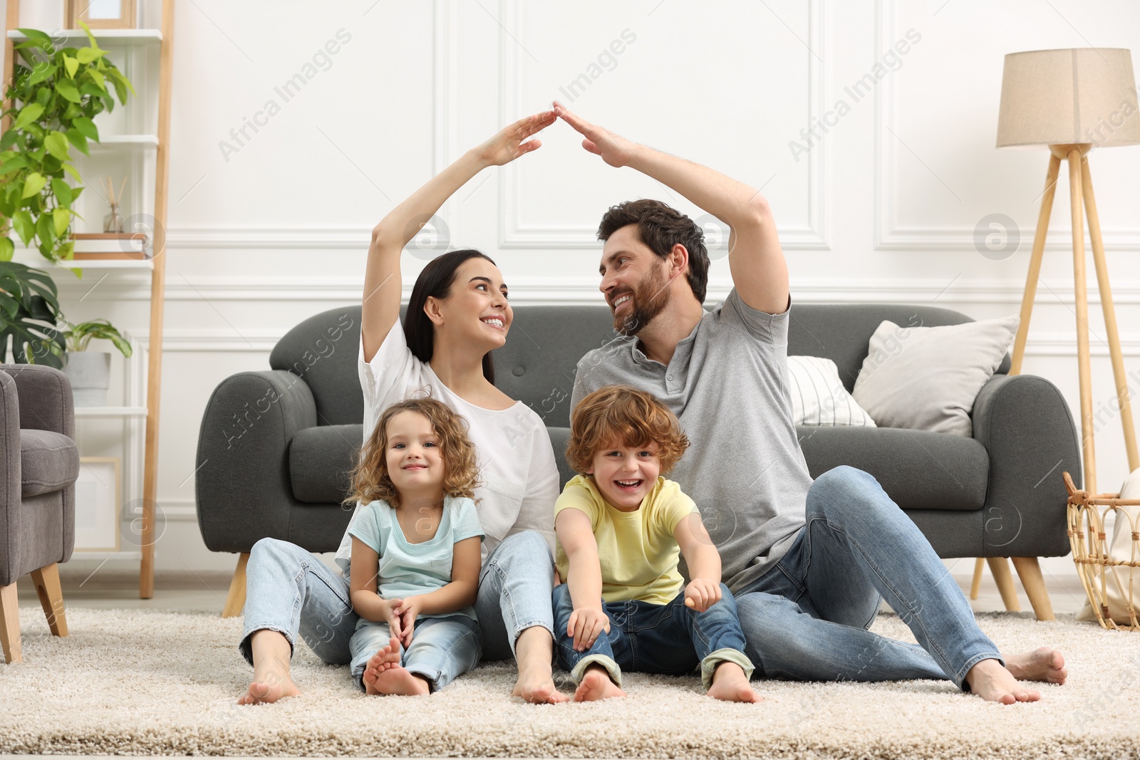 Photo of Family housing concept. Happy woman and her husband forming roof with their hands while sitting with kids on floor at home