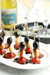 Tasty canapes with black olives, mozzarella and cherry tomatoes on white marble table, closeup