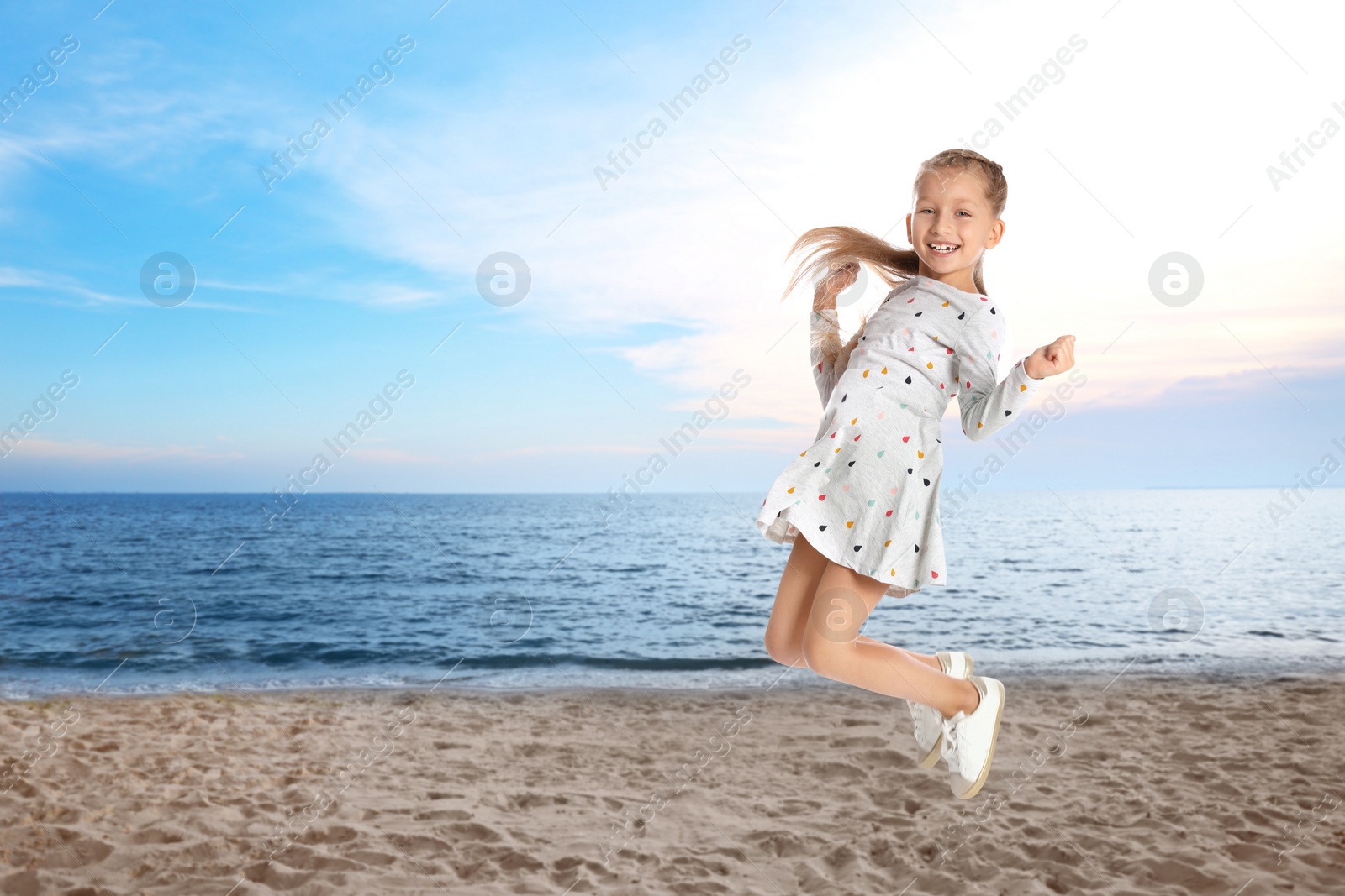 Image of Happy school girl jumping on beach near sea, space for text. Summer holidays