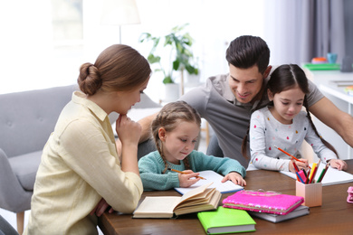 Parents helping their daughters with homework at table indoors