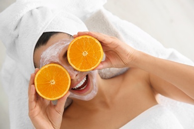 Photo of Pretty woman with rejuvenating facial mask holding sliced orange in spa salon, above view