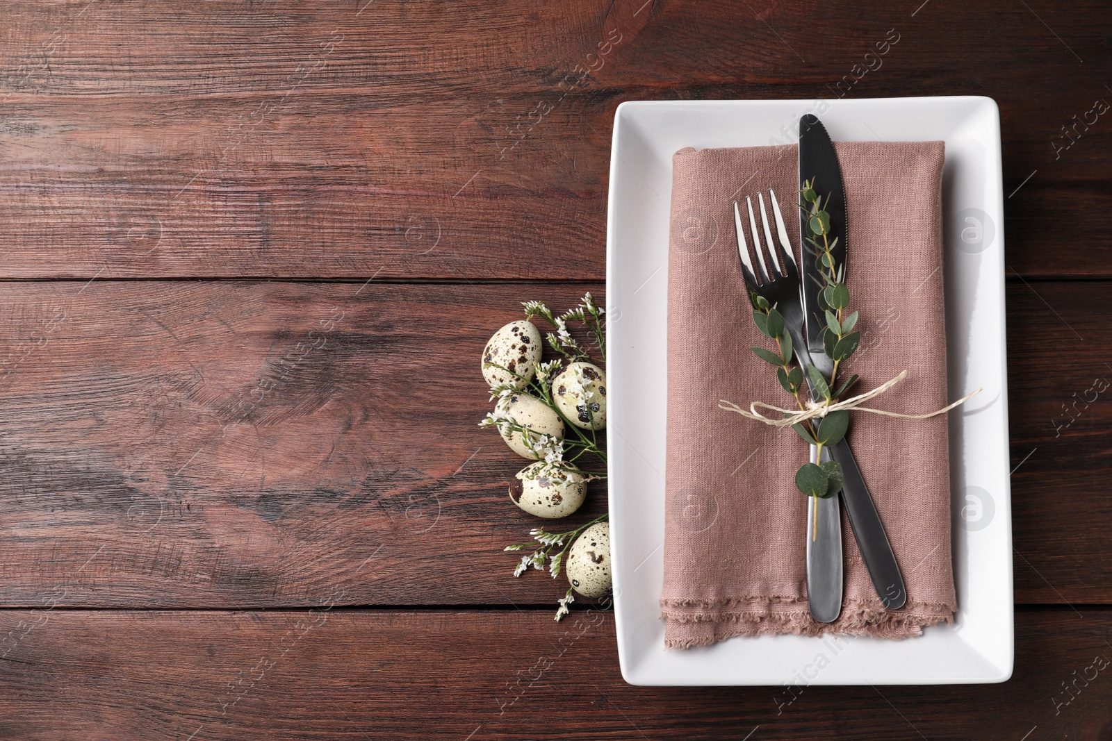 Photo of Festive Easter table setting with quail eggs and floral decor on wooden background, flat lay. Space for text