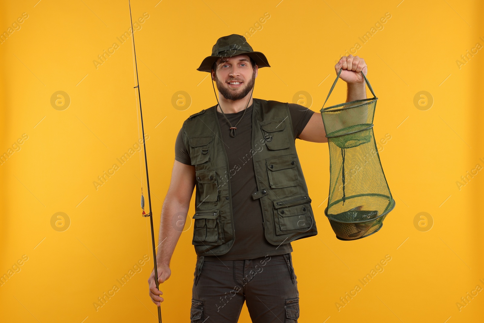 Photo of Fisherman holding rod and fishing net with catch on yellow background