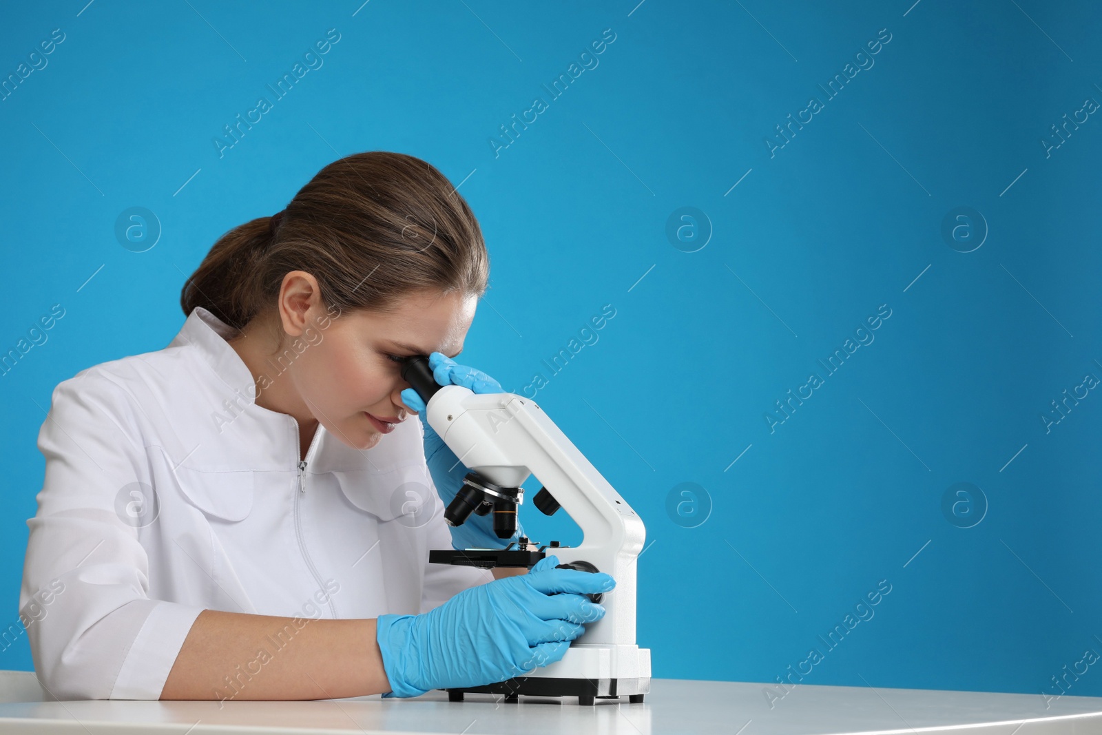 Photo of Scientist using modern microscope at table against blue background, space for text. Medical research