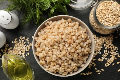 Photo of Tasty pearl barley porridge in bowl on dark table, flat lay