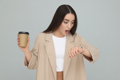 Photo of Shocked young female intern with cup of drink on grey background