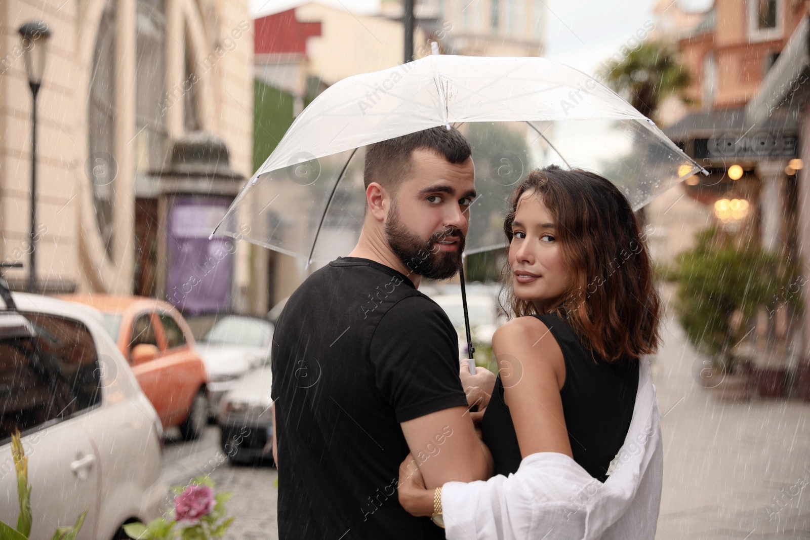 Photo of Young couple with umbrella enjoying time together under rain on city street