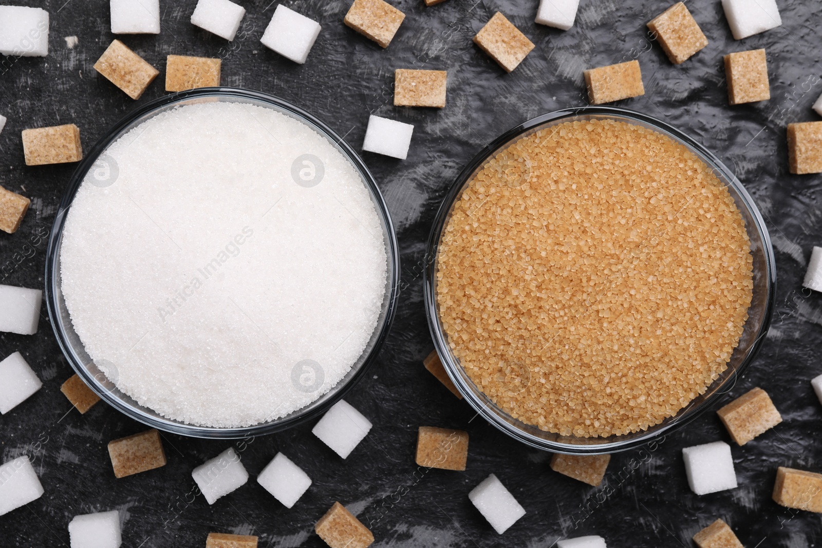 Photo of Different types of sugar in bowls on dark gray textured table, flat lay