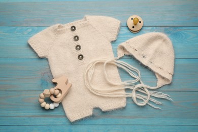 Photo of Baby pacifier, toy, knitted romper and hat on light blue wooden background, flat lay