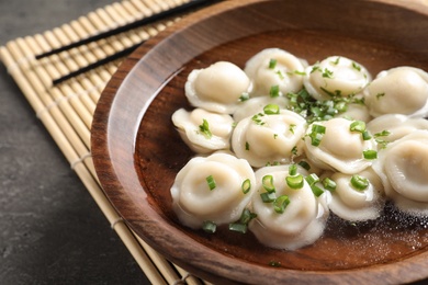 Photo of Bowl of tasty dumplings in broth on table, closeup